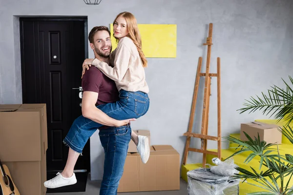 Alegre hombre sosteniendo en brazos complacido novia en nuevo hogar - foto de stock