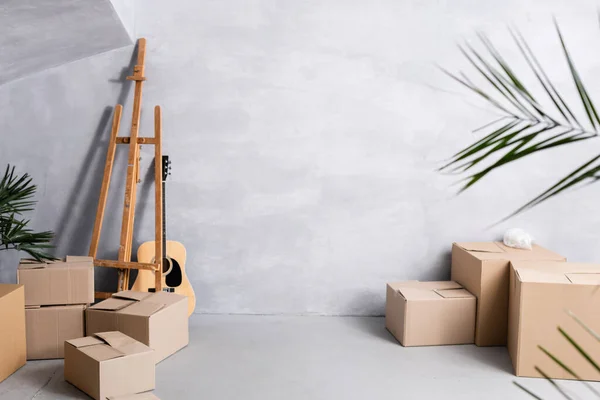 Carton boxes near easel, acoustic guitar and plants — Stock Photo