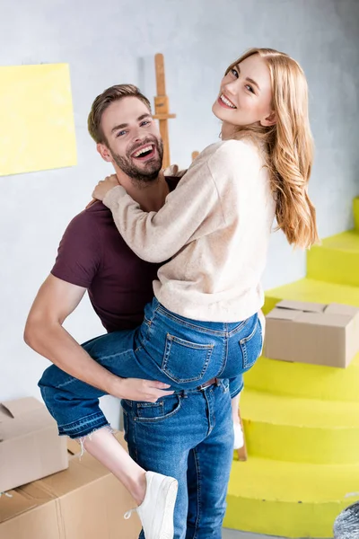 Pleased man holding in arms pleased woman near carton boxes and yellow stairs — Stock Photo