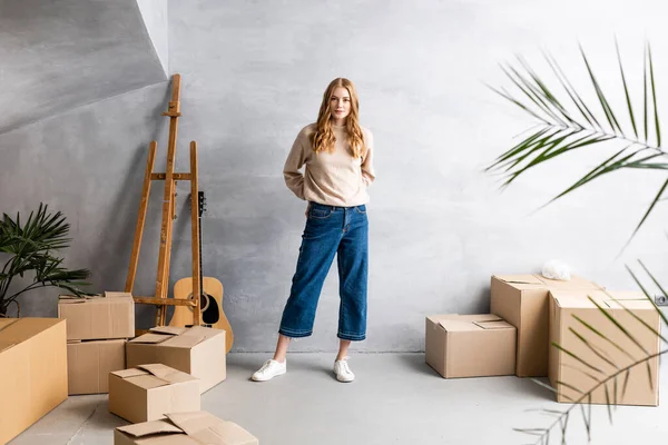 Jovem mulher de pé perto de caixas de papelão e guitarra acústica, conceito de realocação — Fotografia de Stock