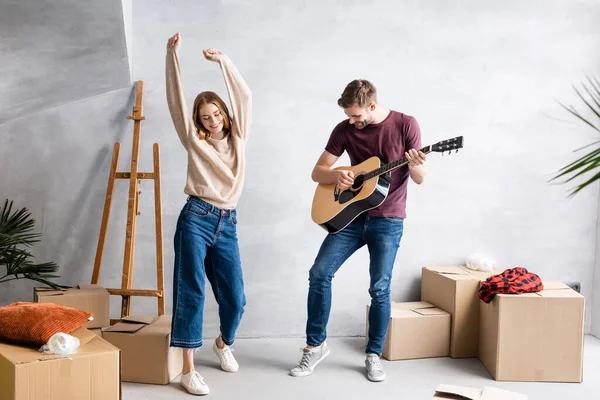 Man playing acoustic guitar near pleased woman dancing with hands above head — Stock Photo