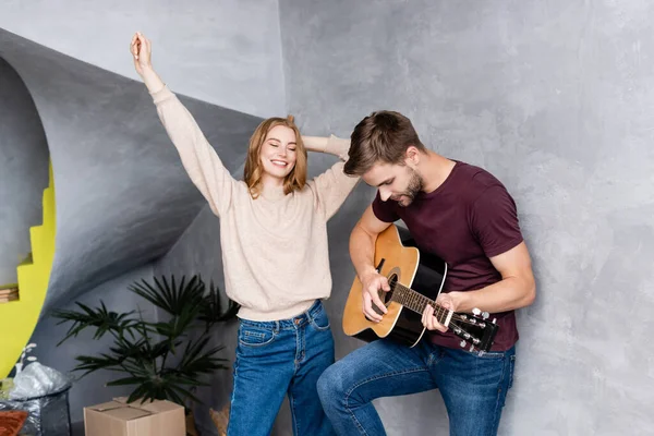 Мужчина играет на акустической гитаре рядом с довольной женщиной, танцующей с рукой над головой — стоковое фото