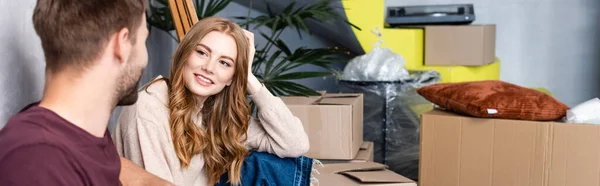 Concepto panorámico de mujer complacida mirando al hombre cerca de cajas, concepto de reubicación - foto de stock