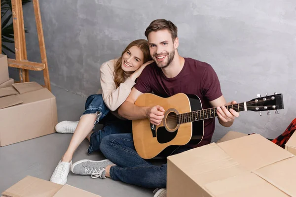 Zufriedene Frau umarmt Freund spielt Akustikgitarre in der Nähe von Boxen, Umzugskonzept — Stockfoto