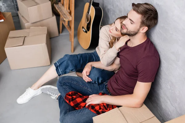 Blick von oben auf zufriedenen Mann, der auf dem Boden sitzt und Freundin in der Nähe von Kisten umarmt — Stockfoto