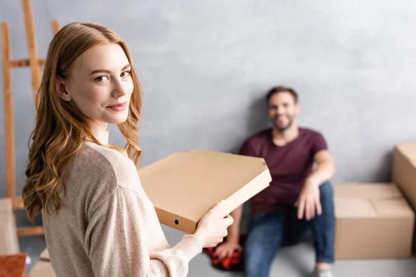 Enfoque selectivo de la mujer joven sosteniendo caja de pizza de cartón cerca de novio - foto de stock