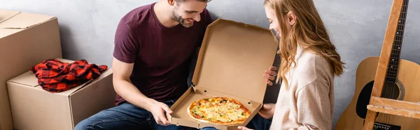 Concepto panorámico de hombre y mujer mirando pizza en caja de cartón - foto de stock