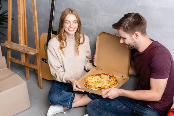 Femme joyeuse regardant petit ami près de pizza, boîtes en carton et guitare acoustique — Photo de stock