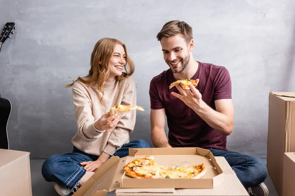 Joyful woman looking at man while holding pizza in new home — Stock Photo