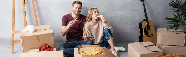 Panoramaaufnahme einer Frau beim Pizza essen in der Nähe von Mann und Kartons, Umzugskonzept — Stockfoto