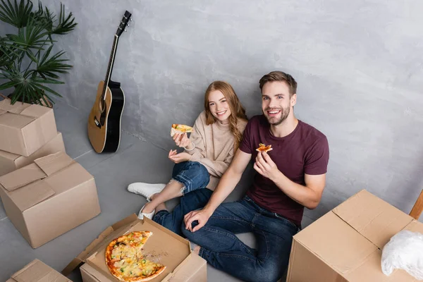 Pareja sentada en el suelo cerca de cajas de cartón y sabrosa pizza - foto de stock