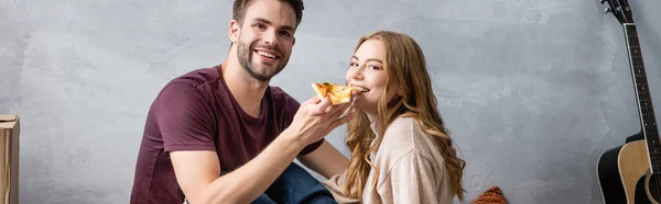 Panoramic concept of pleased man feeding girlfriend with pizza — Stock Photo