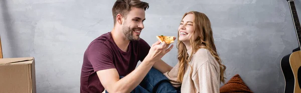 Горизонтальное изображение радостного мужчины, держащего вкусную пиццу рядом с девушкой — стоковое фото
