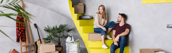 Panoramic shot of man and woman sitting on stairs near boxes, relocation concept — Stock Photo