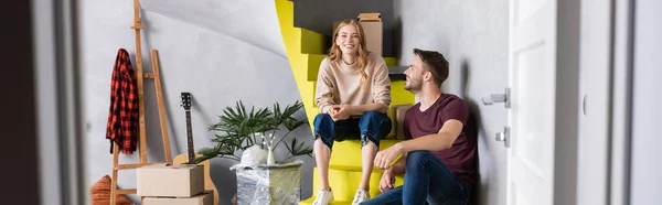 Panoramic crop of man and woman sitting on stairs near boxes, relocation concept — Stock Photo