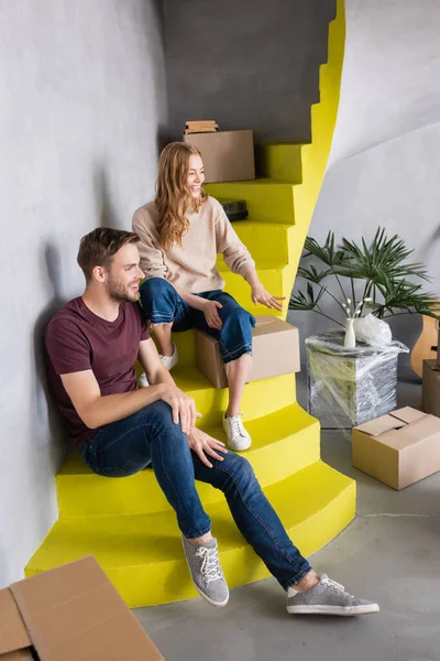 Alegre pareja mirando cajas mientras está sentado en amarillo escaleras - foto de stock