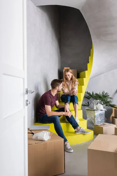 Селективное внимание молодой пары, сидящей на лестнице рядом с коробками, концепция переселения — стоковое фото