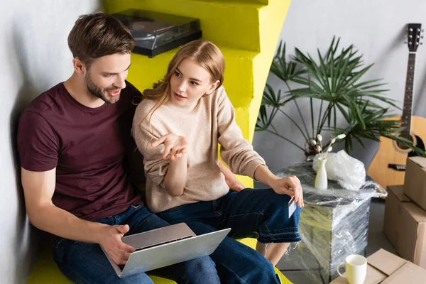 High angle view of woman pointing with hand while holding credit card near boyfriend using laptop — Stock Photo