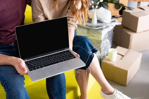 Vista cortada de casal segurando laptop com tela em branco enquanto sentado em escadas perto de caixas, conceito de realocação — Fotografia de Stock