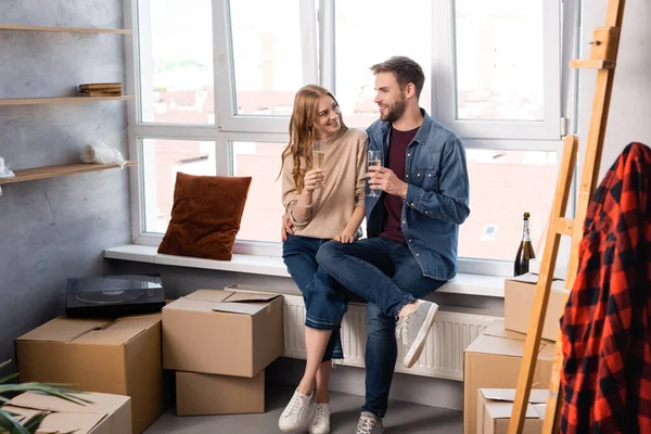 Pleased woman and man holding glasses with champagne near carton boxes — Stock Photo