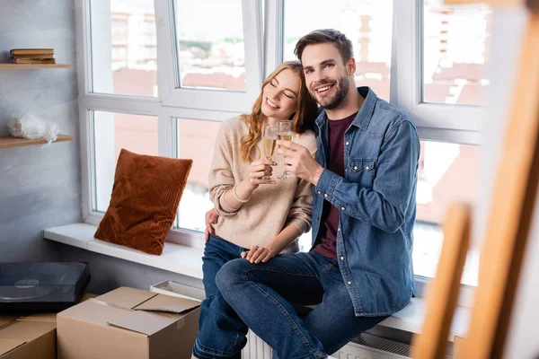 Selective focus of pleased man and woman clinking glasses with champagne near carton boxes, moving concept — Stock Photo