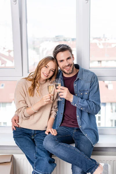 Pleased man and woman clinking glasses with champagne near carton boxes, moving concept — Stock Photo