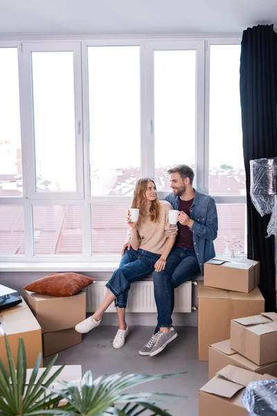 Heureux couple tenant tasses avec thé près des boîtes en carton, concept mobile — Photo de stock