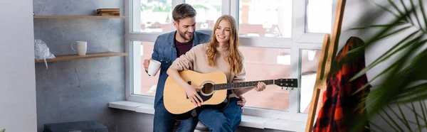 Панорамный снимок женщины, играющей на акустической гитаре рядом с мужчиной — стоковое фото