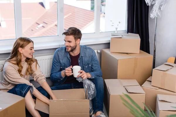 Enfoque selectivo del hombre sosteniendo la taza y desempacando la caja con la novia, concepto móvil - foto de stock