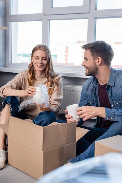 Selektiver Fokus der Frau mit Becher und Auspacken der Schachtel mit Freund, bewegendes Konzept — Stockfoto