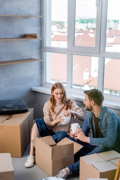 Selective focus of young woman unpacking box with boyfriend, moving concept — Stock Photo