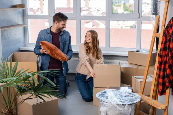 Joyeux homme tenant oreiller près des boîtes de déballage femme, concept mobile — Photo de stock