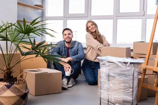 Hombre y mujer mirando la cámara cerca de cajas de cartón, concepto en movimiento - foto de stock