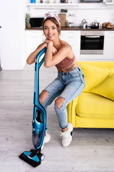 Housewife looking at camera while leaning on vacuum cleaner at home — Stock Photo