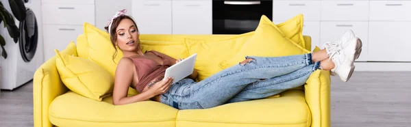Панорамная ориентация женщины лежащей на желтом диване с цифровым планшетом — стоковое фото