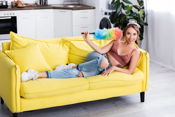 Young housewife holding dust brush while lying on couch at home — Stock Photo