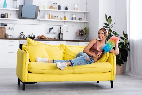 Housewife holding dust brush while lying on sofa at home — Stock Photo