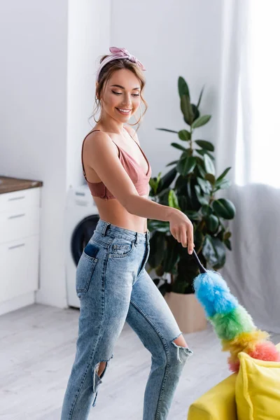 Concentration sélective de la jeune femme nettoyage canapé jaune avec brosse à poussière à la maison — Photo de stock