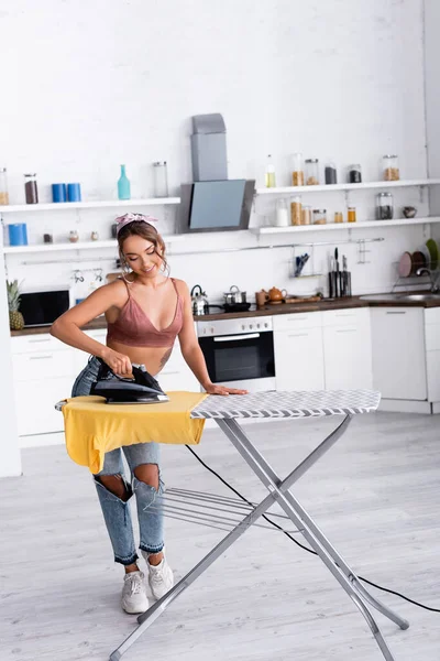 Jovem dona de casa engomar t-shirt na tábua de engomar na cozinha — Fotografia de Stock