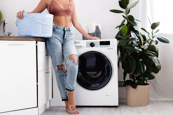 Ausgeschnittene Ansicht einer barfüßigen Frau mit Wäschekorb neben der Waschmaschine bei der Hausarbeit zu Hause — Stockfoto