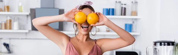 Website-Kopfzeile einer Frau, die zu Hause Orangen in der Nähe der Augen hält — Stockfoto