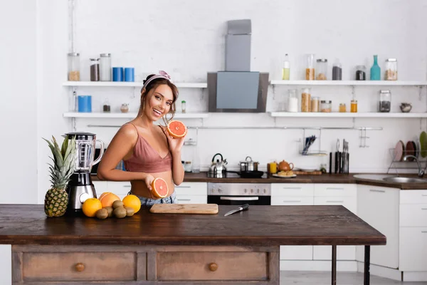 Enfoque selectivo de la mujer sosteniendo mitades de pomelo mientras hace batido en la cocina — Stock Photo