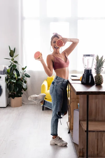 Concentration sélective de la femme au foyer tenant des moitiés de pamplemousse près de l'ananas et du mélangeur sur la table — Photo de stock