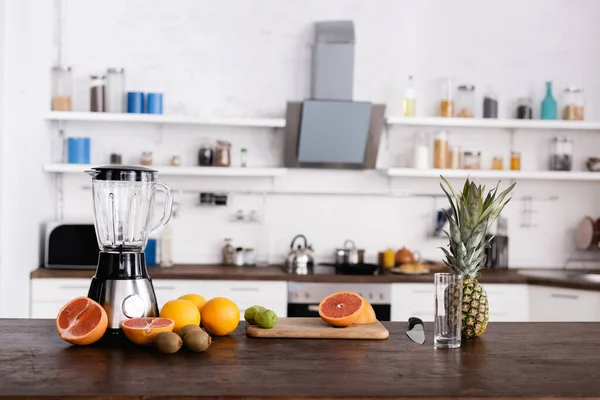 Fresh fruits on cutting board near glass and blender on kitchen table — Stock Photo