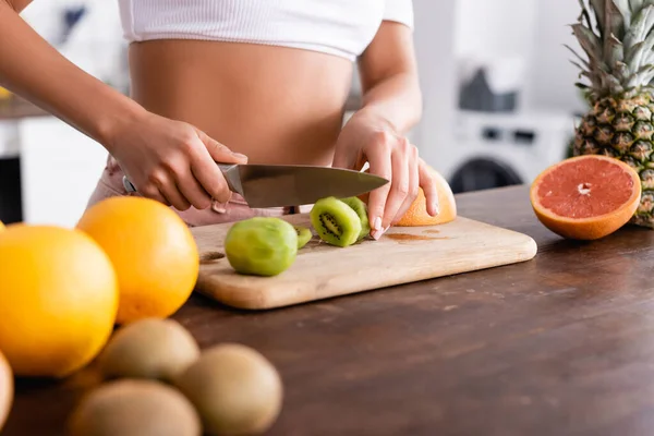 Cropped view of young woman cutting kiwi near fresh fruits on table — Stock Photo