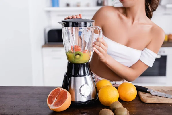 Cropped view of woman preparing smoothie from fresh fruits in kitchen — Stock Photo