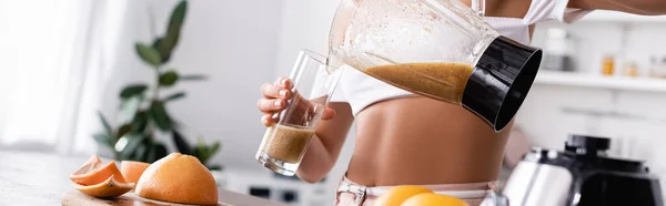 Imagem horizontal da mulher derramando smoothie em vidro na cozinha — Fotografia de Stock