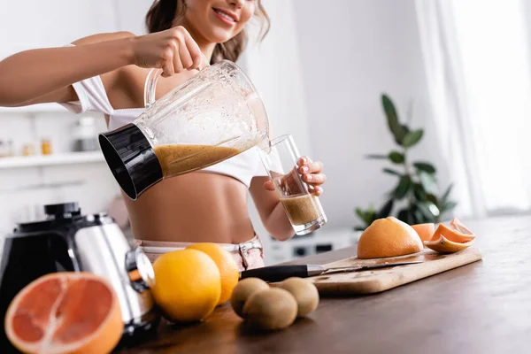 Обрізаний вигляд молодої жінки, що наливає смужку в склянку біля органічних фруктів на кухонний стіл — стокове фото