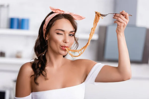 Junge Frau zwinkert in die Kamera, während sie zu Hause Spaghetti isst — Stockfoto
