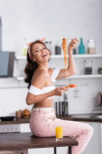 Vue latérale de la jeune femme tenant des spaghettis assis sur la table de cuisine — Photo de stock